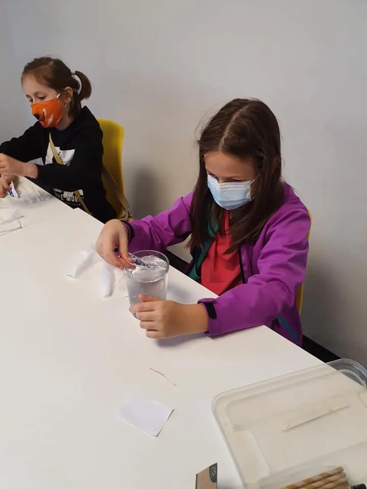 Fetiță care lucrează la un experiment cu un pahar de apă