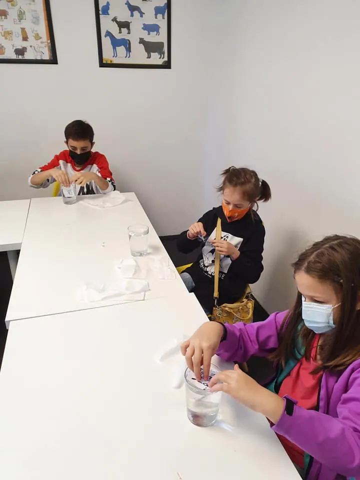 Trei copii care lucrează la experimente cu pahare și șervețele