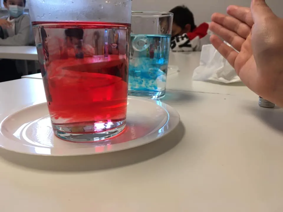 Pahare cu apă colorată în roșu și albastru, pe farfurii