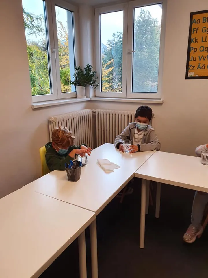 Copii la masă în sala atelierului, lângă fereastră